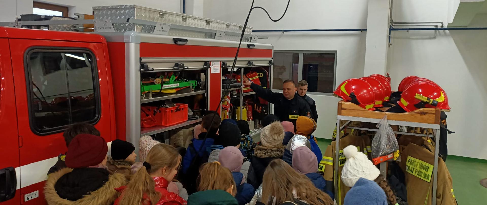 Odwiedziny w ramach akcji „Odwiedź strażnicę i salę edukacyjną typu Ognik” w KP PSP w Sokołowie Podlaskim - na zdjęciu dzieci zapoznają się z pojazdami i wyposażeniem znajdującym się w jednostce, przed czerwonym samochodem strażackim.