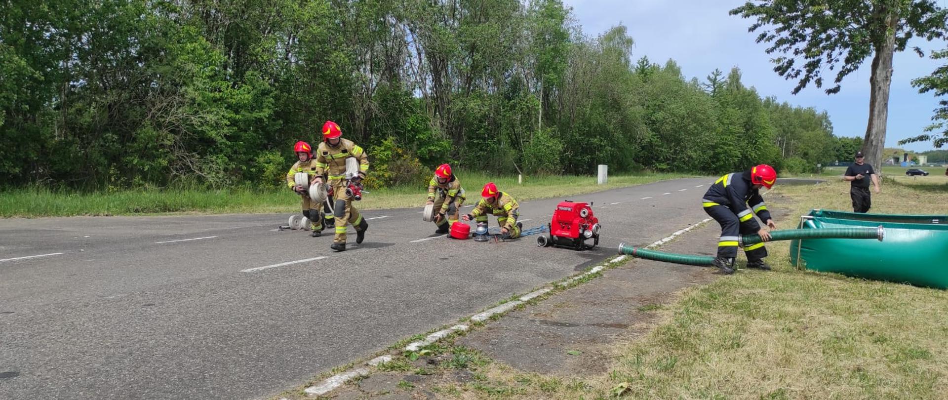 Zdjęcie przedstawia składanie linii ssawnej podczas zawodów przez kilku strażaków.