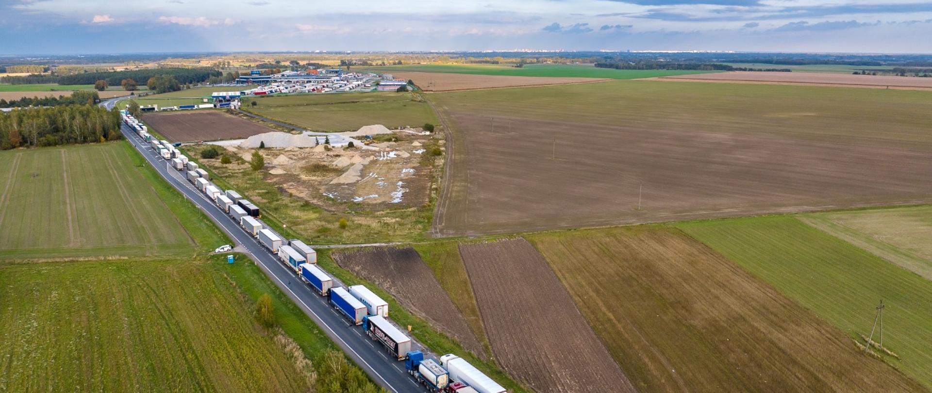 Długa kolejka ciężarówek stojących na jednokierunkowej drodze — pojazdy ustawione są jeden za drugim na kilku kilometrach.