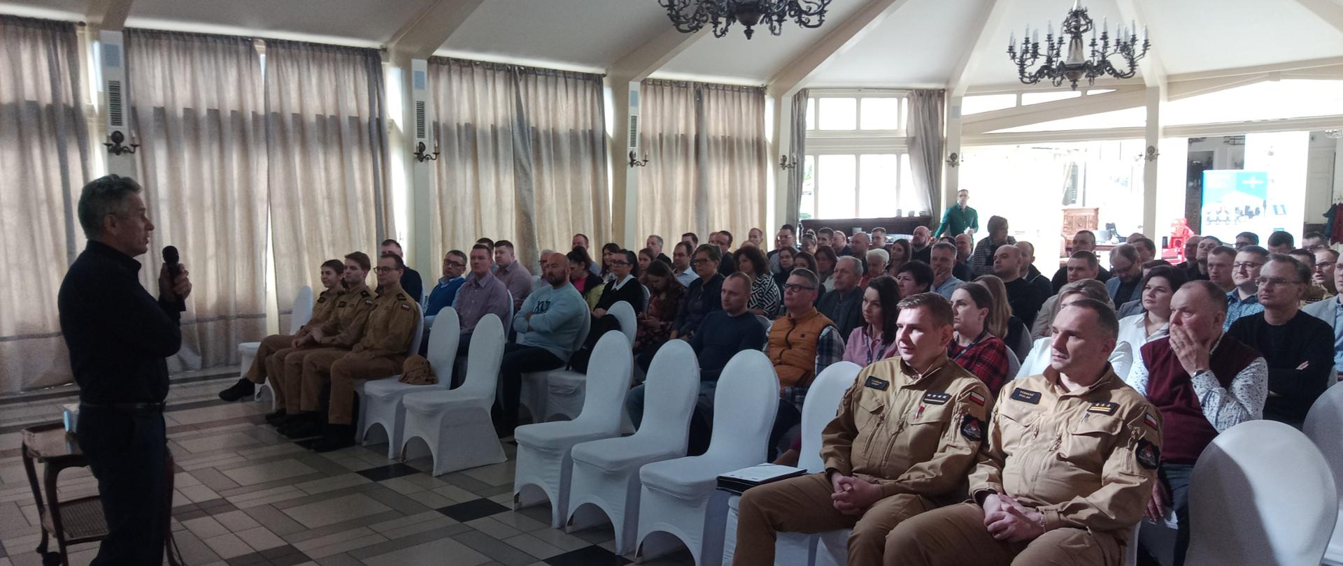 Zdjęcie w pomieszczeniu. Widać osoby siedzące na krzesłach. 