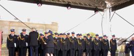Strażacy stoją na scenie i odbierają akty nadania wyższego stopnia służbowego 