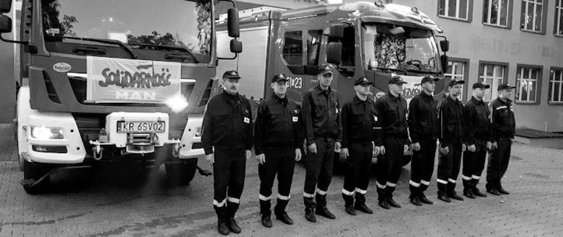 Na zdjęciu strażacy w umundurowaniu koszarowym przed samochodami pozarniczymi