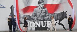 Premier RP Mateusz Morawiecki, europosłanka Jadwiga Wiśniewska oraz Patrycja Słocińska na tle ściany z muralem, który właśnie uroczyście odsłonili