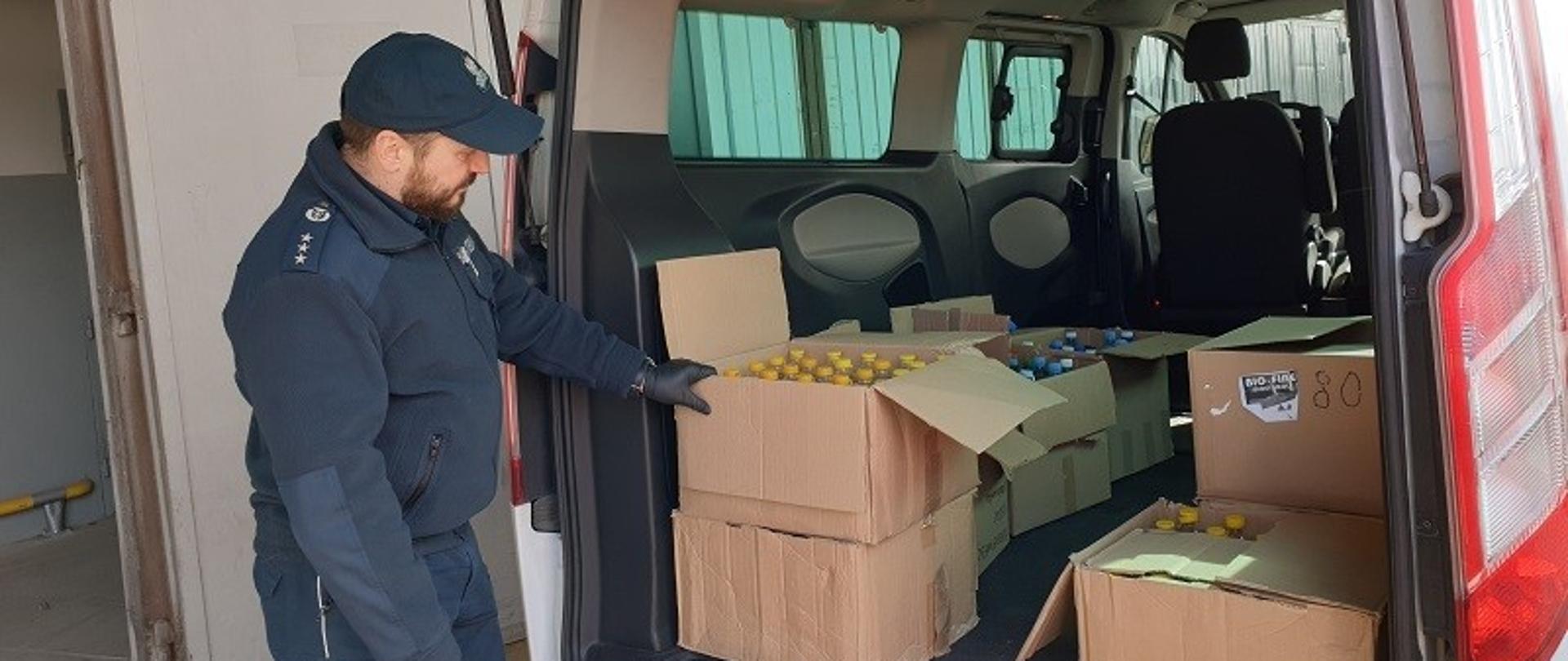 Funkcjonariusz KAS przy otwartym samochodzie dostawczym, w którym znajdują się kartony z przekazanym alkoholem.