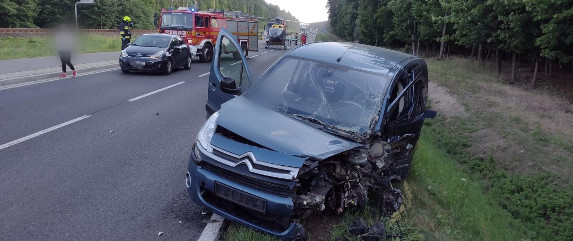 Na zdjęciu widać rozbity pojazd osobowy oraz w tle śmigłowiec LPR oraz służby ratunkowe 