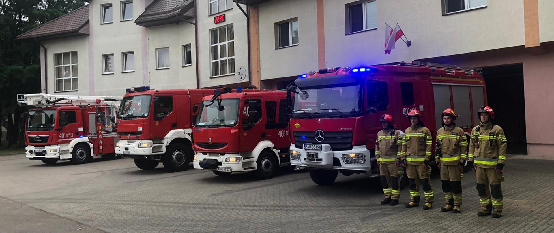 Na zdjęciu strażacy przy samochodach z włączonymi sygnałami świetlnymi i dźwiękowymi
