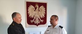 strażacy podajacy sobie dłonie w tle godło polski