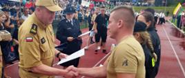 Widok z boku. Zastępca Małopolskiego Komendanta Wojewódzkiego PSP wręcza pamiątkowy dyplom za udział w wydarzeniu kapitanowi jednej z drużyn 