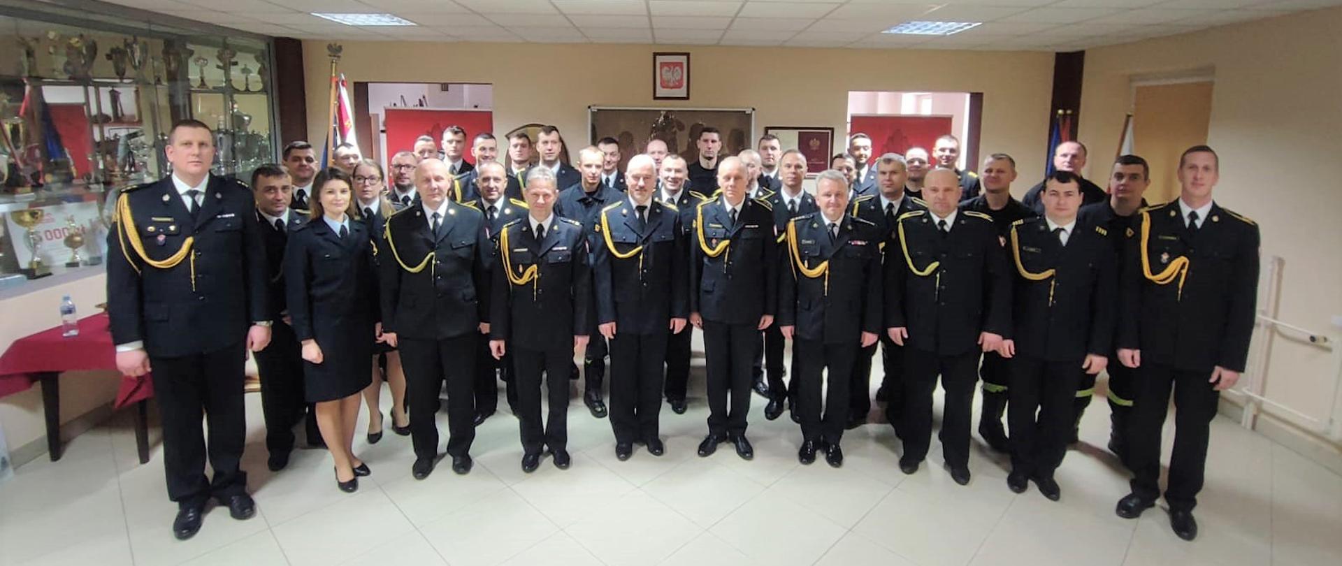 W dniu 3 lutego 2023 r. odbyła się uroczysta zbiórka, podczas której Komendant Powiatowy Państwowej Straży Pożarnej w Przasnyszu st. bryg. Waldemar Białczak, podziękował za wieloletnią służbę asp.sztab. Andrzejowi Kupiszewskiemu oraz st.ogn. Krzysztofowi Morawskiemu, którzy z dniem 31 stycznia 2023 r. przeszli na zasłużone zaopatrzenie emerytalne.
Uroczystość odbyła się w obecności Sztandaru Komendy Powiatowej PSP w Przasnyszu i licznie przybyłych koleżanek i kolegów, Życzącym świeżo upieczonym emerytom wszystkiego najlepszego na nowym etapie życia.
Nie obyło się też bez chwil wzruszenia i uśmiechu, podczas przemówień podsumowujących i upamiętniających dorobek służby obu wspaniałych strażaków. Na zakończenie uroczystości odchodzącym na zaopatrzenie emerytalne funkcjonariuszom wręczono symboliczne upominki.
asp.sztab. Andrzej Kupiszewski służbę w ochronie przeciwpożarowej rozpoczął w 1991 r. jako kadet Szkoły Chorążych Pożarnictwa w Poznaniu. Po ukończeniu Szkoły rozpoczął służbę stałą w Komendzie Rejonowej PSP w Przasnyszu w dniu 2 sierpnia 1993 r. na stanowisku technika w służbie kontrolno-rozpoznawczej. W latach 1995-1998 prowadził sprawy kadrowo-organizacyjne na stanowisku inspektora i starszego inspektora. 31 grudnia 2001 r. został mianowany kierownikiem sekcji w wydziale operacyjno szkoleniowym. W latach 2007-2017 pełnił służbę w Stanowisku Kierowania Komendanta Powiatowego jako dyżurny operacyjny powiatu. Od czerwca 2017 r. do 31.01.2023r. ponownie pełnił służbę w codziennym rozkładzie czasu służby jako starszy inspektor w samodzielnym stanowisku pracy ds. kadrowo-organizacyjnych.
Był strażakiem o odpowiednich kwalifikacjach, rzetelnej wiedzy, doświadczeniu oraz dużych umiejętnościach praktycznych. Sumiennie wykonywał obowiązki służbowe wynikające z jego obszernego zakresu czynności. Cechowała go samodzielność, kreatywność oraz zaangażowanie w pracy nad powierzonymi zagadnieniami. Był funkcjonariuszem uczynnym, konsekwentnie dążącym do realizacji założonych celów oraz dającym przykład młodszym strażakom. Cieszył się zaufaniem przełożonych i szacunkiem współpracowników.
Odznaczony Srebrną Odznaką Zasłużony dla Ochrony Przeciwpożarowej, Złotym Medalem za Zasługi dla Pożarnictwa.
st.ogn. Krzysztof Morawski po przebyciu postępowania kwalifikacyjnego rozpoczął służbę przygotowawczą w Komendzie Rejonowej PSP w Przasnyszu w dniu 15.07.1997 r. na stanowisku stażysty. Następnie, już w służbie stałej w latach 1999-2004 na stanowiskach młodszy ratownik i ratownik. Z dniem 1.12.2004 r. został mianowany ratownikiem-kierowcą a następnie starszym ratownikiem – kierowcą. W latach 2011 – 2021 pracował na stanowisku operatora sprzętu specjalnego i starszego operatora sprzętu. W roku 2022 mianowany został na dowódcę zastępu w JRG KP PSP w Przasnyszu.
Przez cały okres swej służby związany był z pionem operacyjnym JRG pełniąc funkcje na stanowiskach wymagających obsługi specjalistycznego sprzętu pożarniczego i posiadał do tego wszelkie uprawnienia i kwalifikacje. Był pracownikiem sumiennym, zdyscyplinowanym, dbał o powierzony sprzęt pożarniczy. Z obowiązków służbowych wywiązywał się wzorowo. Wyróżniał się poświęceniem podczas działań ratowniczo gaśniczych. Dzięki prezentowanym walorom zawodowym i postawie w służbie cieszył się dużym zaufaniem i uznaniem współpracowników oraz przełożonych.
Odznaczony Brązową Odznaką Zasłużony dla Ochrony Przeciwpożarowej, Srebrnym Medalem za Zasługi dla Pożarnictwa
