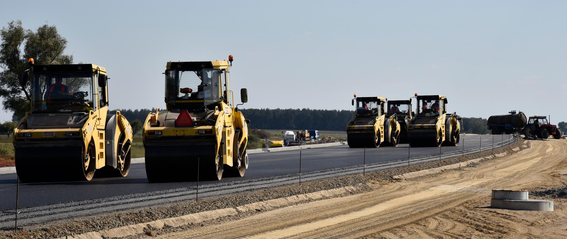 Układanie nawierzchni bitumicznej. Widocznych jest pięć walców zagęszczających masę bitumiczną.