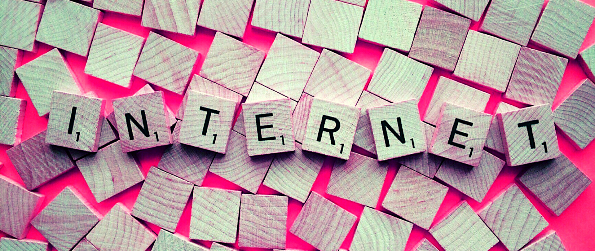 Drewniane klocki na różowym tle. Osiem z nich tworzy napis: INTERNET