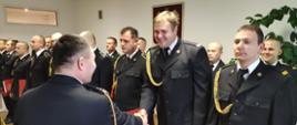Zdjęcie przedstawia funkcjonariuszy podczas uroczystości mianowania na wyższe stanowiska służbowe. Strażacy stojący w dwuszeregu, znajdują się w świetlicy Komendy Powiatowej Państwowej Straży Pożarnej w Lwówku Śląskim. Komendant Powiatowy PSP w Lwówku Śląskim wręcza mianowanie funkcjonariuszowi. 