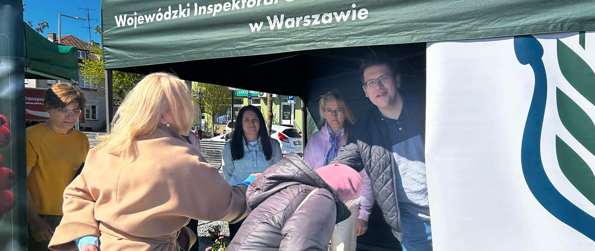 Osoby odwiedzające stoisko WIORiN pod namiotem sięgają po materiały i upominki znajdujące się na stole