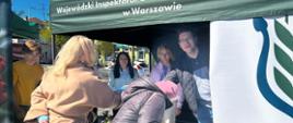 Osoby odwiedzające stoisko WIORiN pod namiotem sięgają po materiały i upominki znajdujące się na stole
