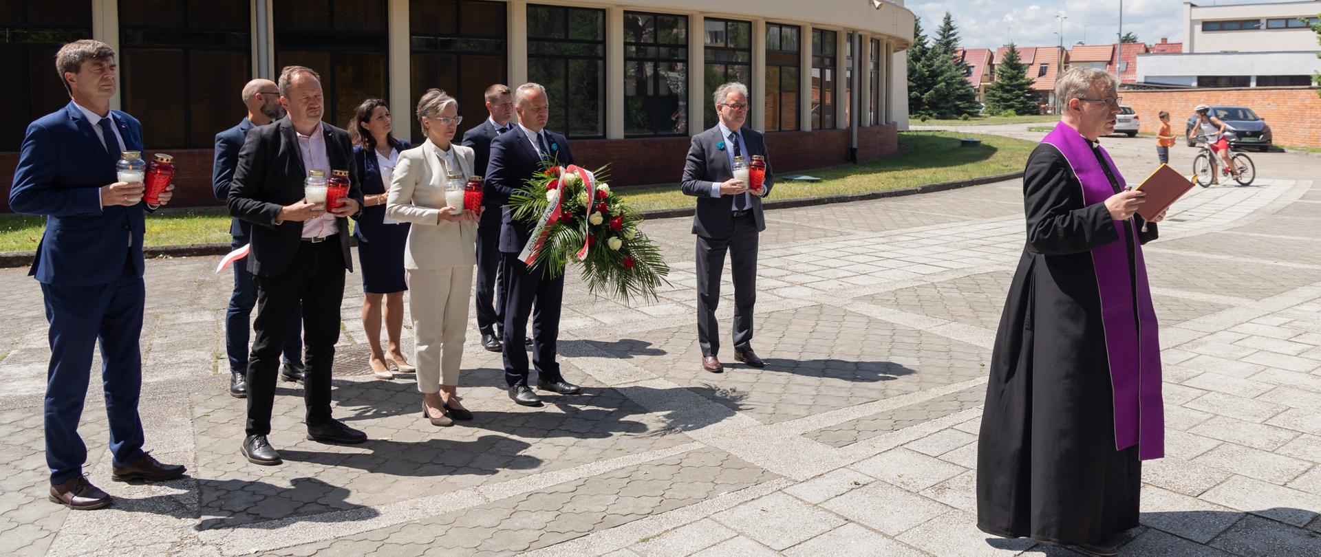 
Grupa ludzi w garniturach z kwiatami i zniczami
