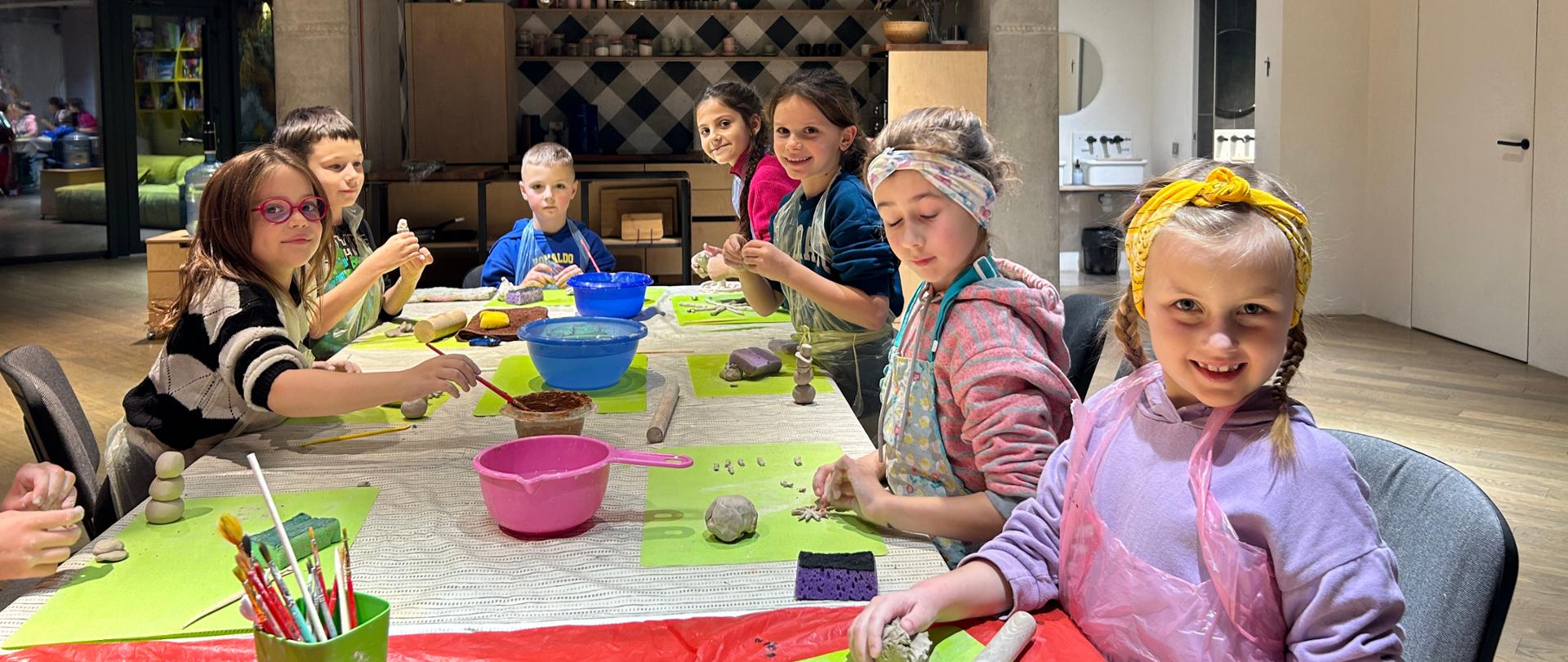 Grupa dzieci przy stole przygotowuje wyroby z gliny