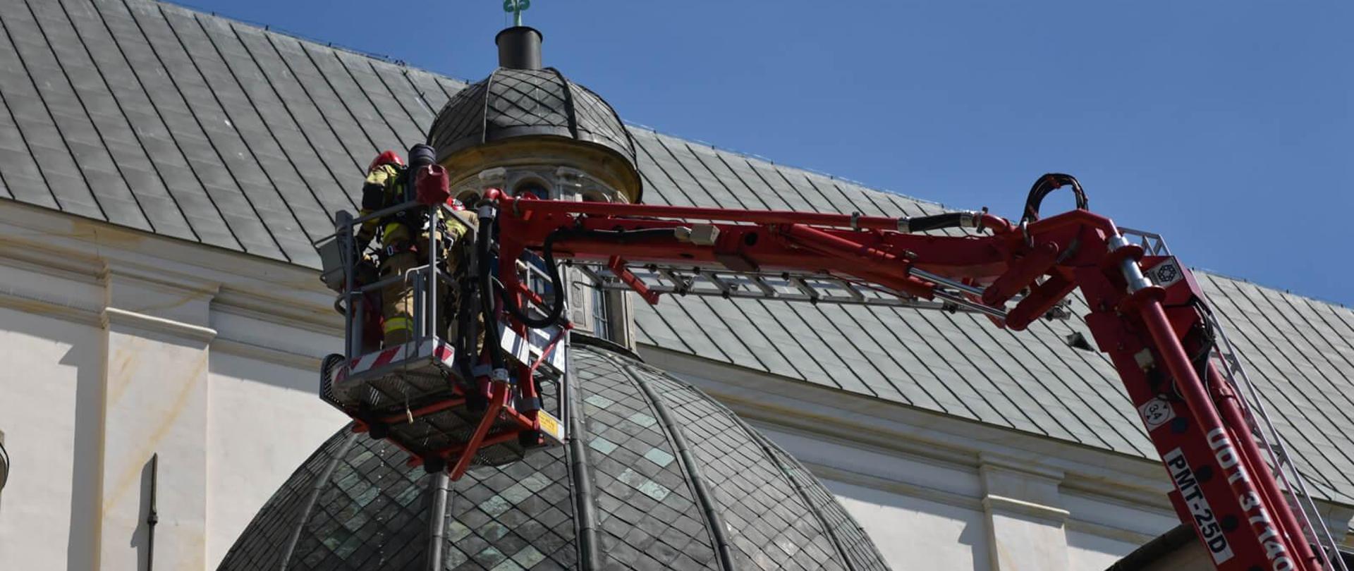 strażacy w koszu podnośnika hydraulicznego na tle dachu katedry