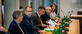 Przy podłużnym stole siedzi kilka osób, wśród nich minister Wieczorek.