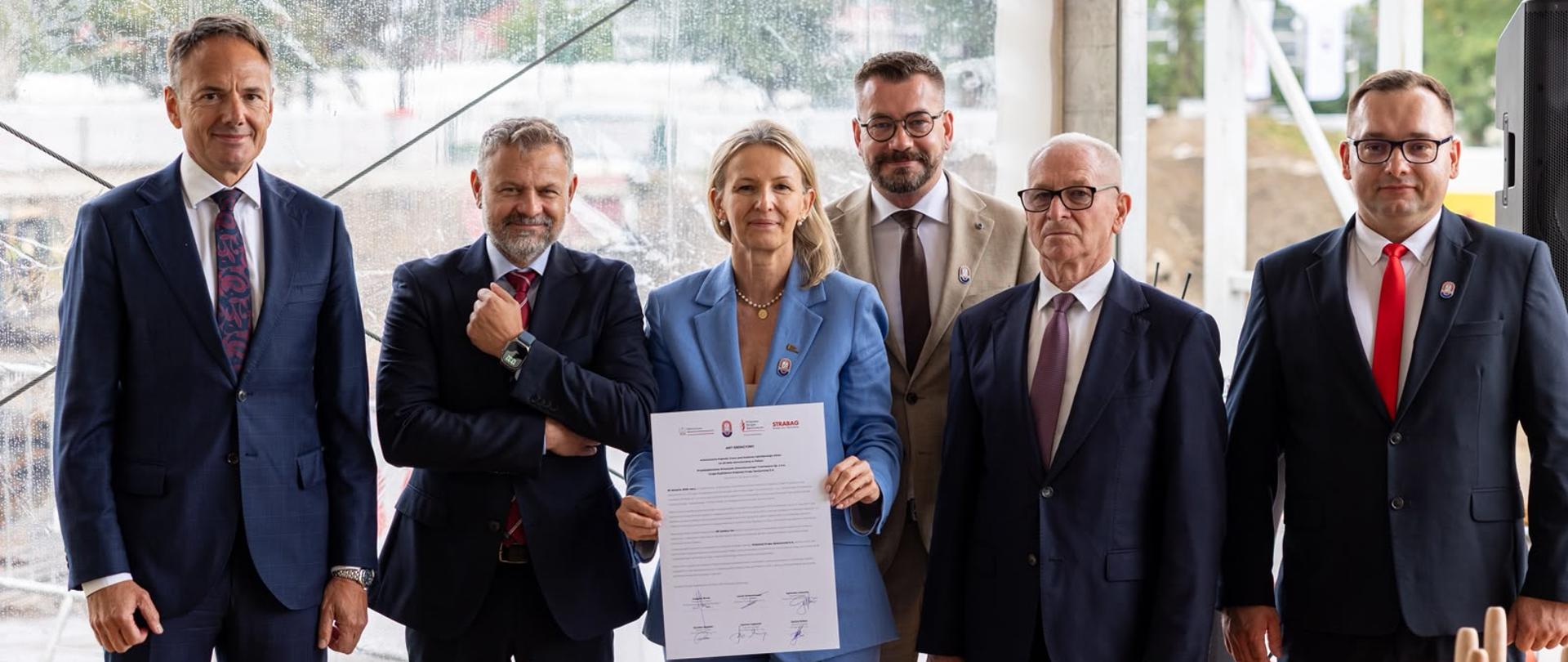 Wiceminister Grzegorz Wrona i inni uczestnicy podczas uroczystości wmurowania Kapsuły Czasu pod budowę inwestycji. 