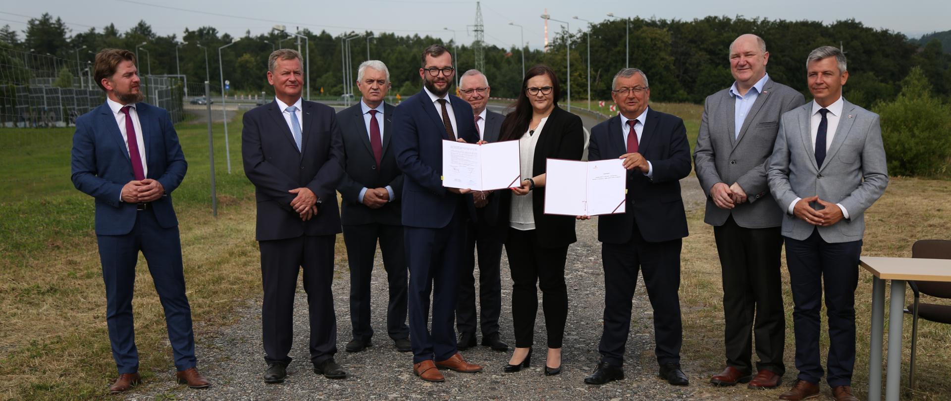 Na zdjęciu stoją uczestnicy podpisania umów na budowę nowego odcinka drogi ekspresowej S1. W środku stoją minister Małgorzata Jarosińska-Jedynak i wiceminister Grzegorz Puda.