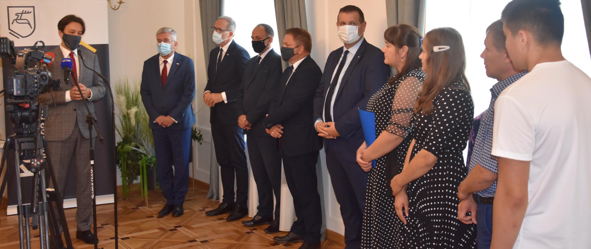 Na zdjęciu widać kobiety i mężczyzn na uroczystości przekazania kluczy repatriantom z Kazachstanu.