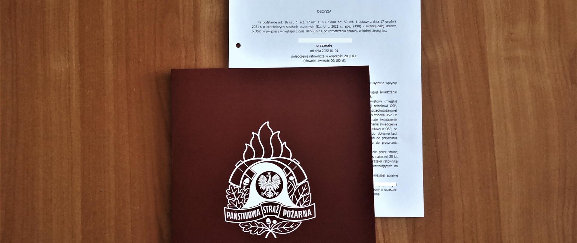 Zdjęcie przedstawia decyzję w sprawie przyznania świadczenia ratowniczego w teczce z logo Państwowej Straży Pożarnej