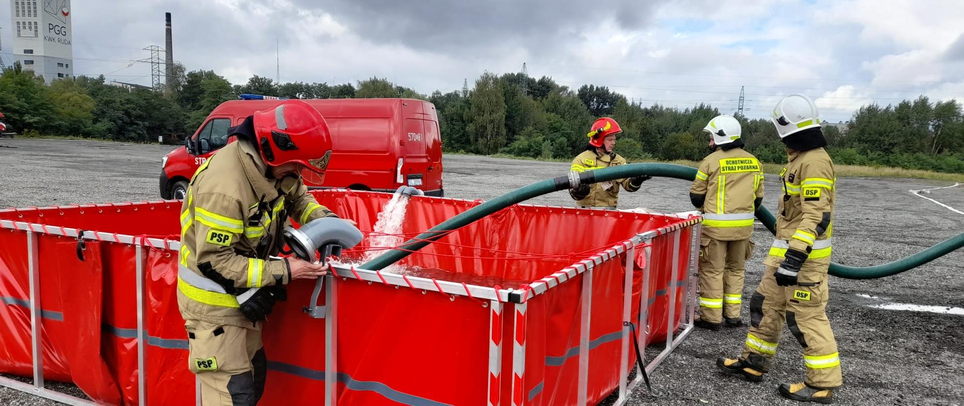 Zdjęcie przedstawia strażaków, którzy podczas ćwiczeń budują stanowisko tzw. bufor wodny.