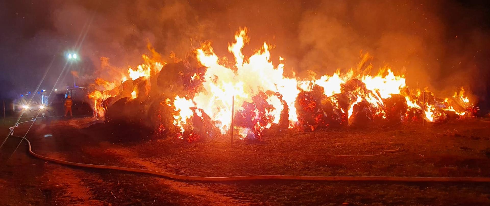 Strażacy nadzorujący i dogaszający palącą się słomę 