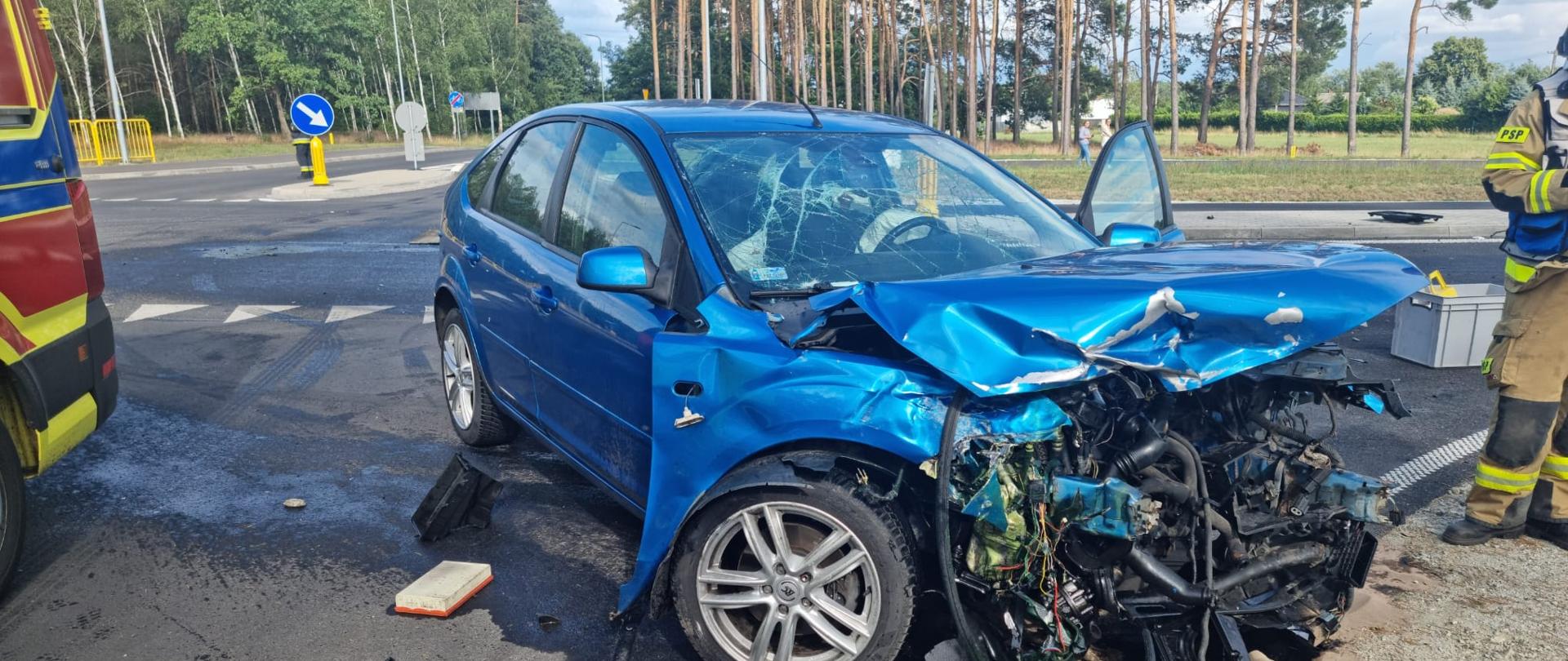 Widać uszkodzony samochód od przodu, jest na drodze