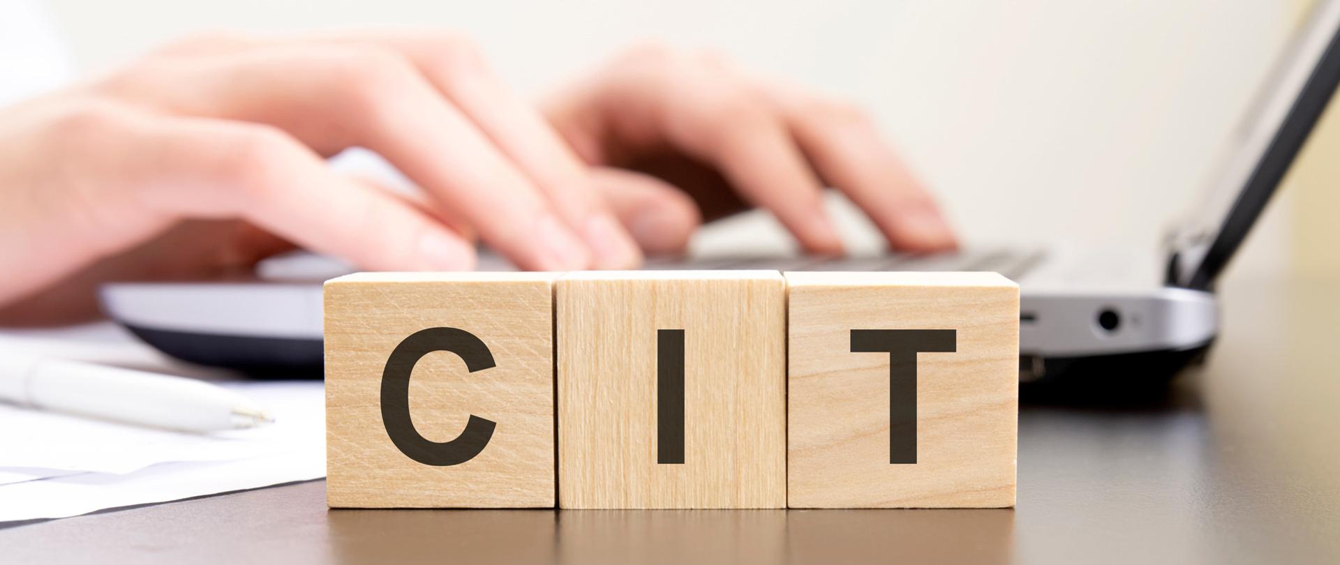 Klocki z literami ułożonymi w napis CIT, dłonie na klawiaturze komputera.