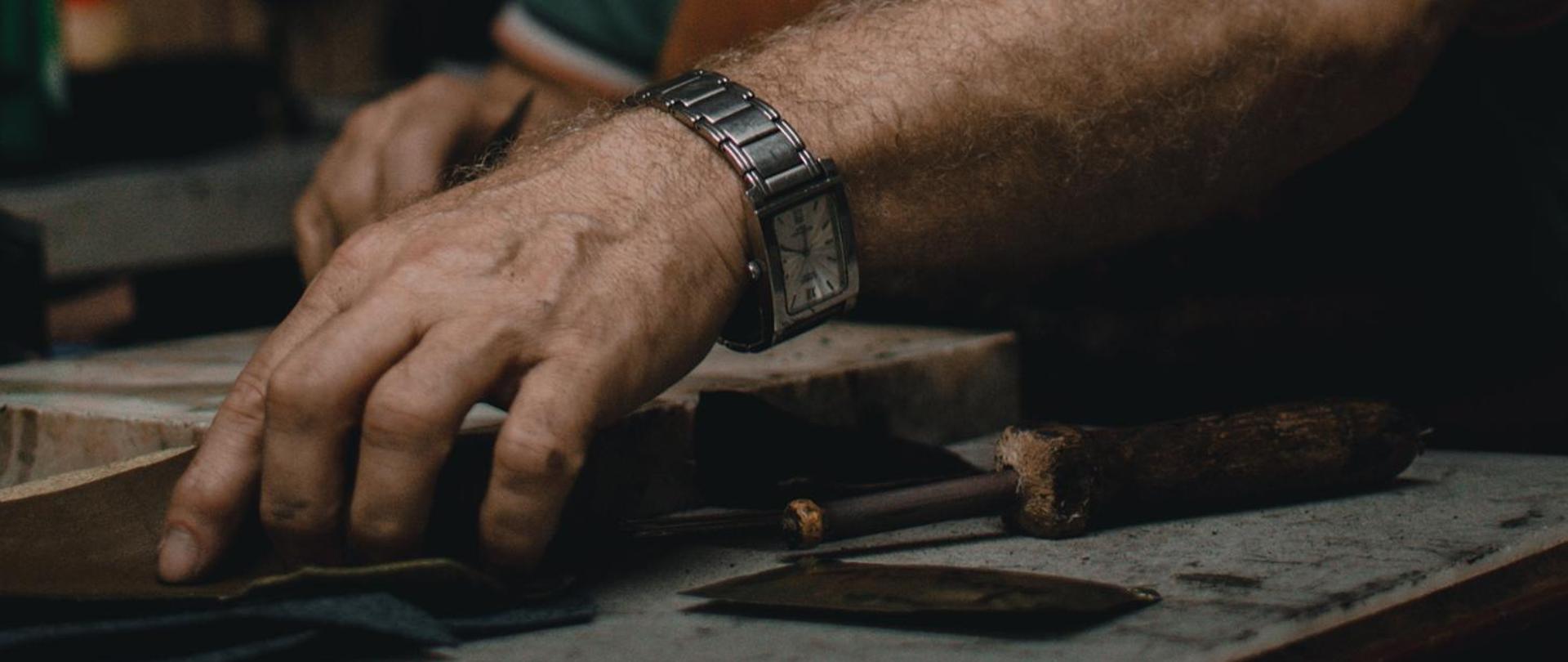 Na pierwszym planie dłoń. Obok dłuto. Domyśleć się można, że jest to człowiek wykonujący prace ręczne.