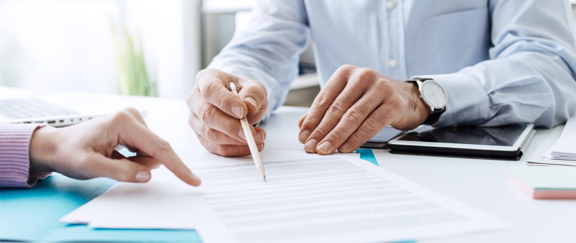 Palce wskazują na dokumenty leżące na stole