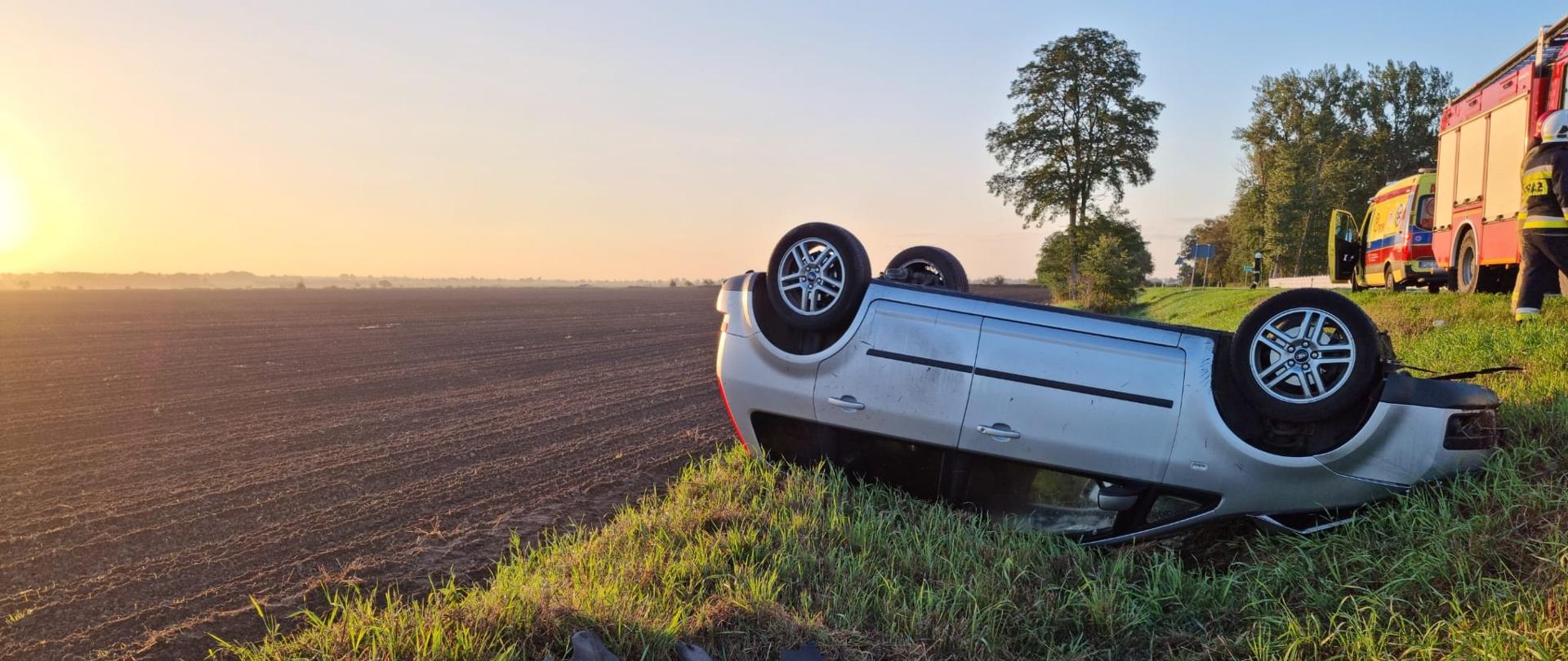 Widać samochód po dachowaniu w rowie, po lewej pole, po prawej samochód straży pożarnej
