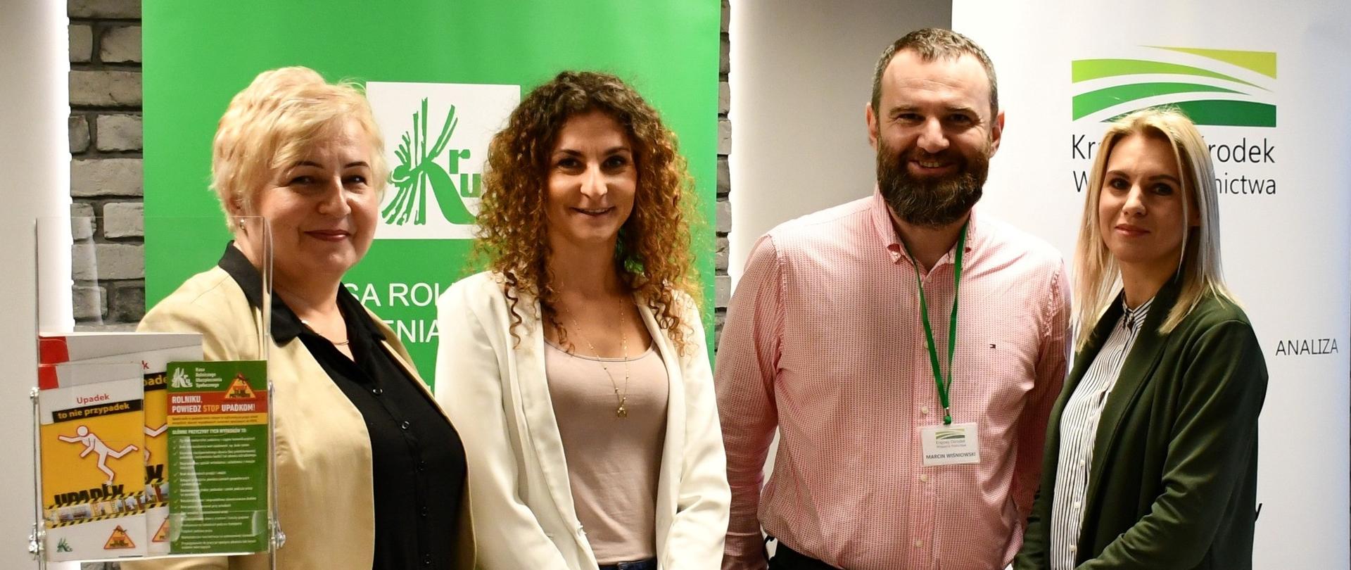 Na tle stoiska informacyjnego KRUS stoją trzy kobiety oraz mężczyzna.