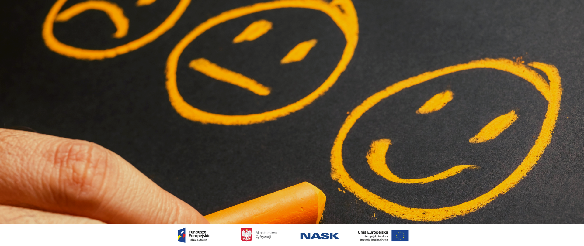 Trzy buźki z różnymi minami narysowane na tablicy pomarańczową kredą. Widać też fragment dłoni trzymającej kredę.