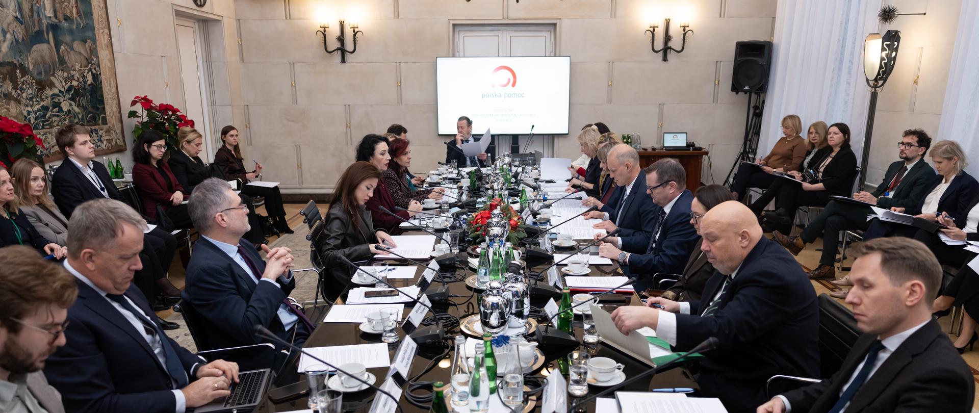 Stół konferencyjny wokół którego siedzą członkowie Rady Programowej, na ekranie widać logo Polskiej pomocy