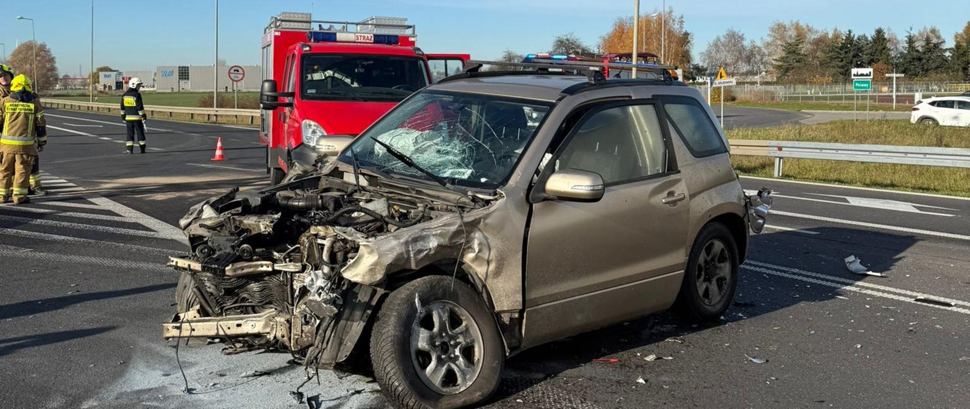 Uszkodzony samochód osobowy na drodze, za nim pojazd strażacki