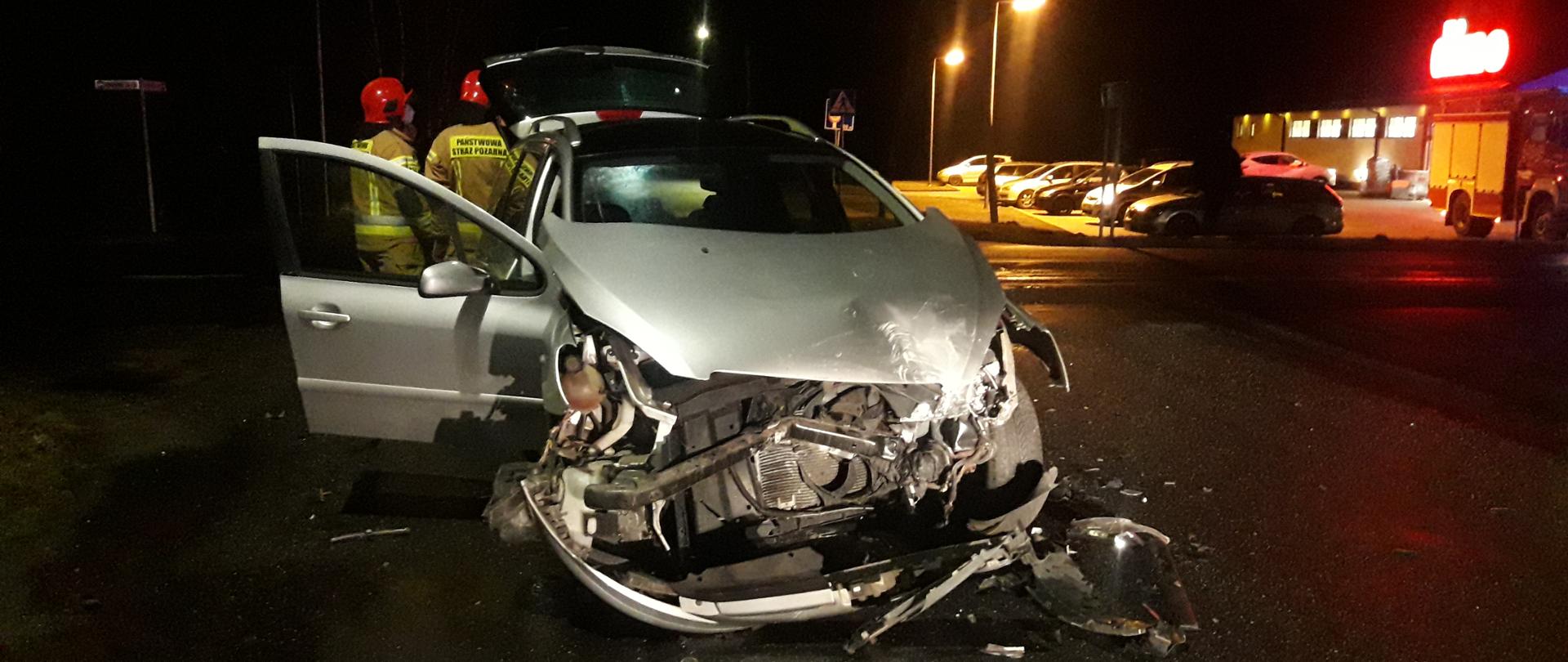 Noc, droga, rozbity samochód, strażacy z tyłu.