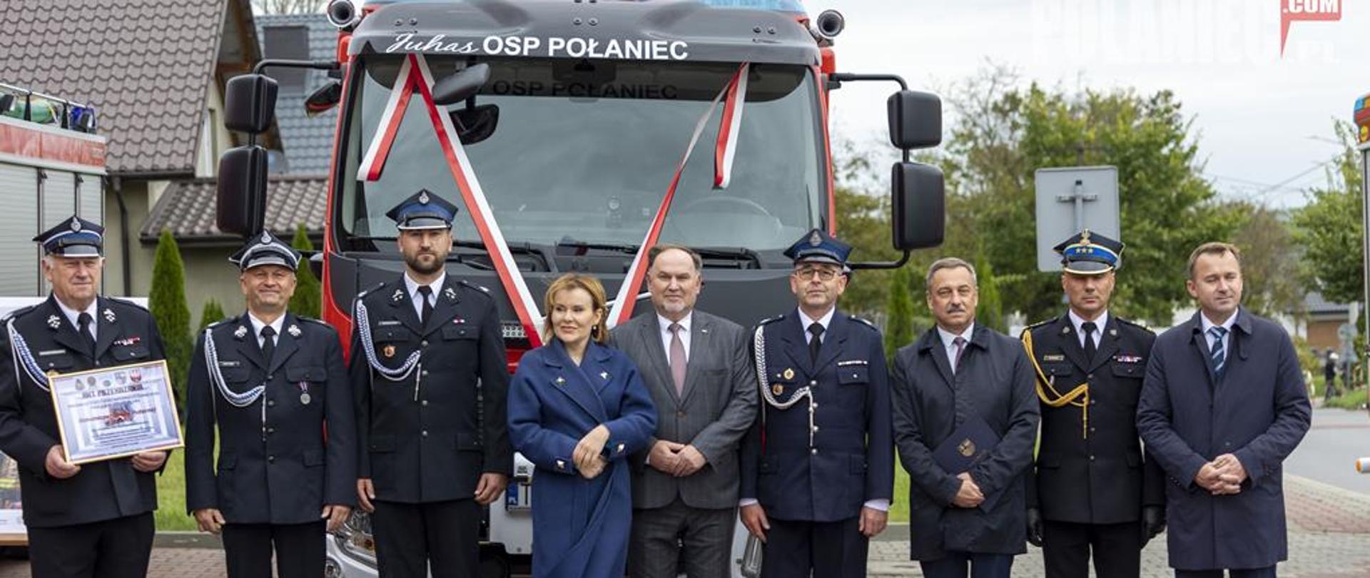 Zaproszenie goście oraz druhowie OSP Połaniec na tle nowego samochodu ratowniczo-gaśniczego.