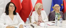 Trzy osoby siedzące przy stole – w środku jest wiceminister edukacji i nauki Marzena Machałek. W tle Flagi Polski i Unii Europejskiej