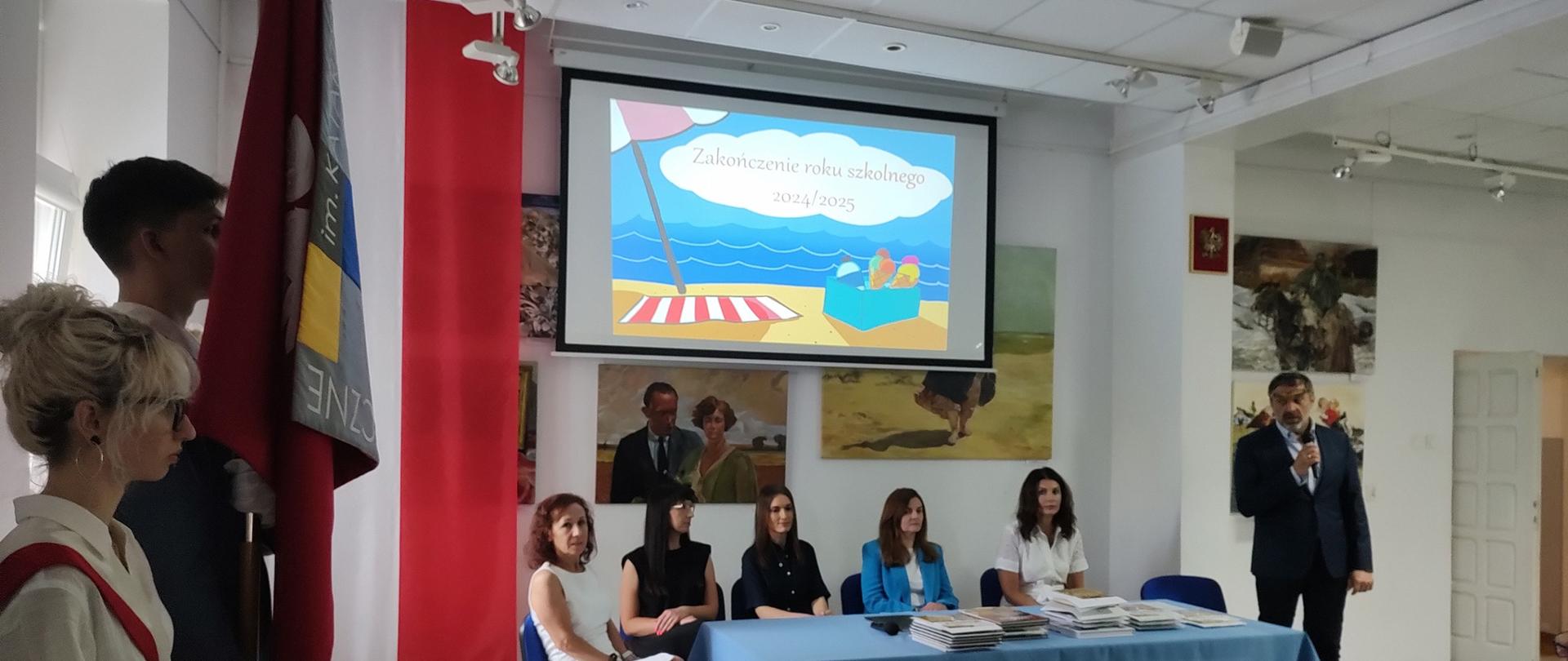 Zdjęcie, na pierwszym planie stół za którym siedzą nauczycielki po lewej stroni widać poczet ze sztandarem szkoły.