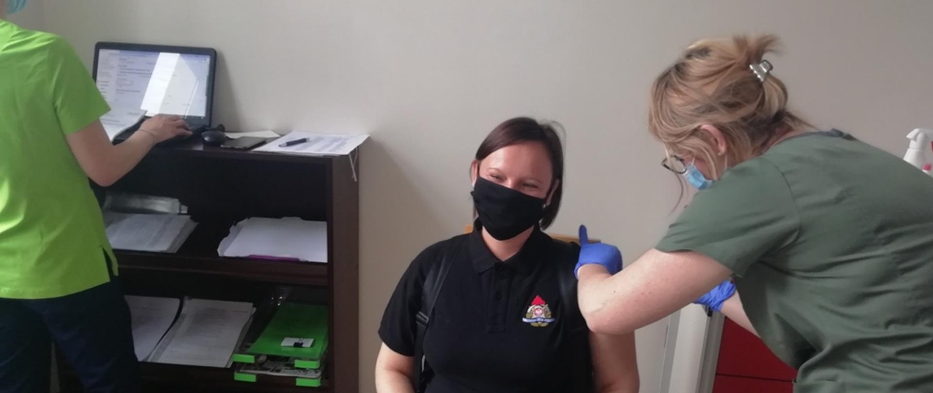 Na zdjęciu funkcjonariuszka Państwowej Straży Pożarnej otrzymującą szczepionkę w punkcie szczepień. Szczepienia dokonuje personel szpitala.