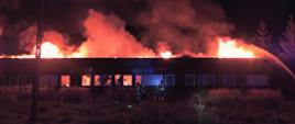 Zdjęcie przedstawia budynek objęty w całości płomieniami. Jest ciemno - widać podawane prądy gaśnicze na tle ognia i dymu. 