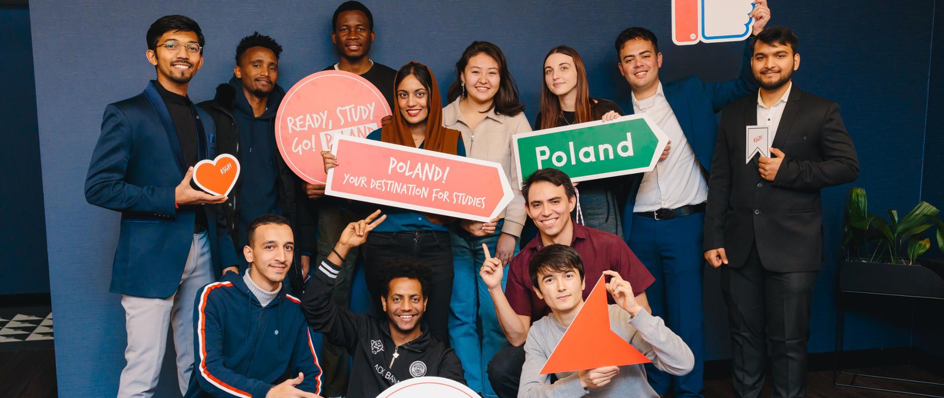 Grupa młodych ludzi pozuje do zdjęcia trzymając banery reklamowe programu stypendialnego