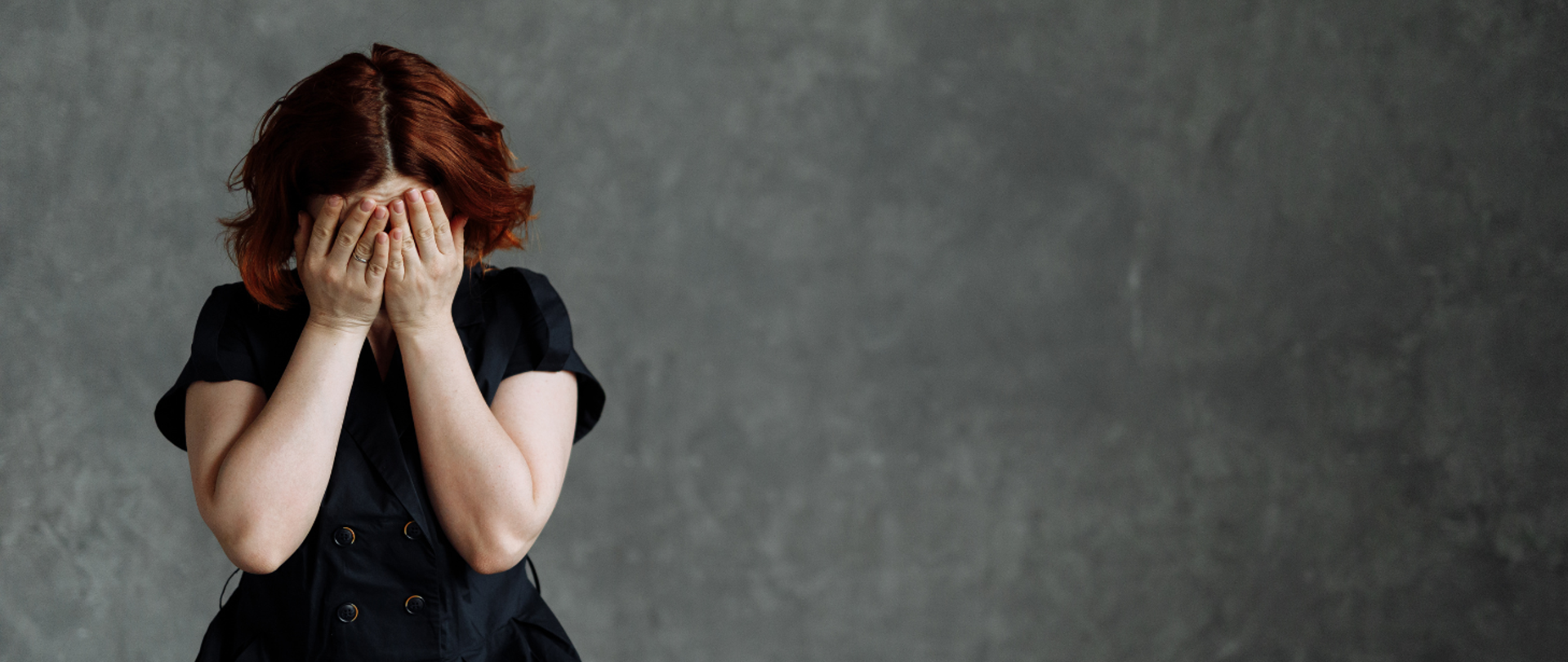 Płacząca kobieta zakrywająca twarz dłońmi na szarym tle