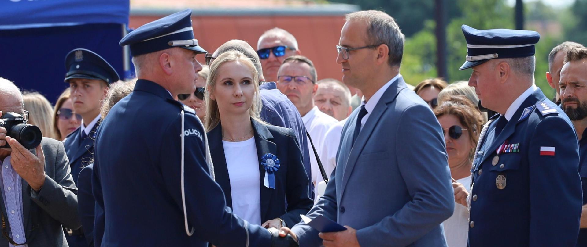 Tłum ludzi. Na pierwszym planie wicewojewoda pomorski podaje rękę komendantowi wojewódzkiemu policji. Obok stoi zastępca komendanta głównego policji.