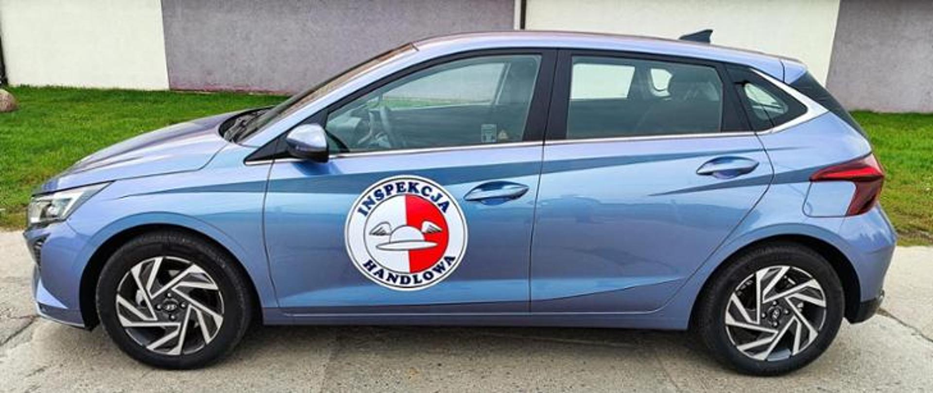 Błękitny samochód osobowy z logiem Inspekcji Handlowej na drzwiach kierowcy.