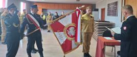 Na zdjęciu znajdują się strażacy w mundurach, Komendant oraz strażak podczas ślubowania. Poczet sztandarowy z opuszczonym sztandarem