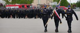 Plac jednostki ratowniczo gaśniczej w Gorzowie Wielkopolskim. Przed jednostką odbywa się uroczystość podczas której wyróżnienia, awansowani i mianowani strażacy z województwa lubuskiego ustawieni są w szeregach. na pierwszym planie z prawej strony maszeruje poczet sztandarowy złożony z trzech strażaków.