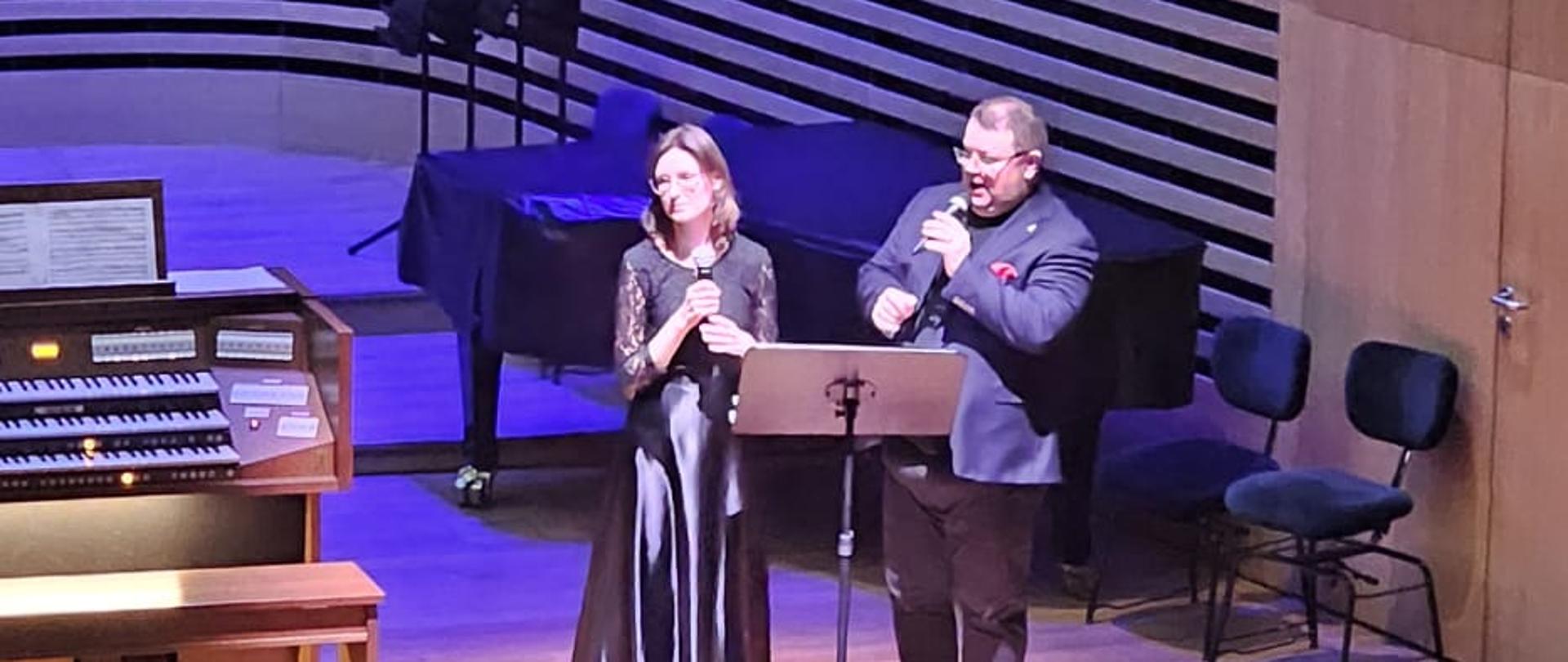 Kobieta i mężczyzna zapowiadają wykonawców.